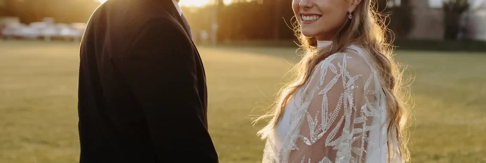 Una pareja de recién casados posando juntos en un campo al atardecer, con el sol creando un hermoso resplandor a su alrededor.