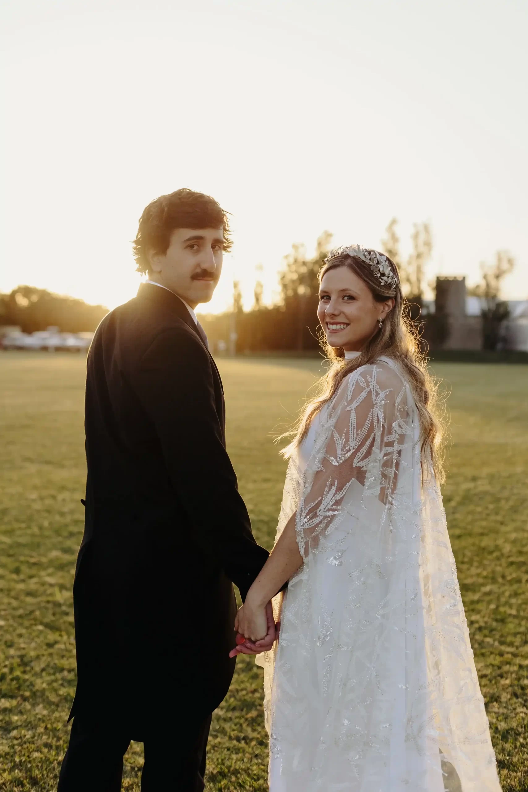 Una pareja de recién casados posando juntos en un campo al atardecer, con el sol creando un hermoso resplandor a su alrededor.