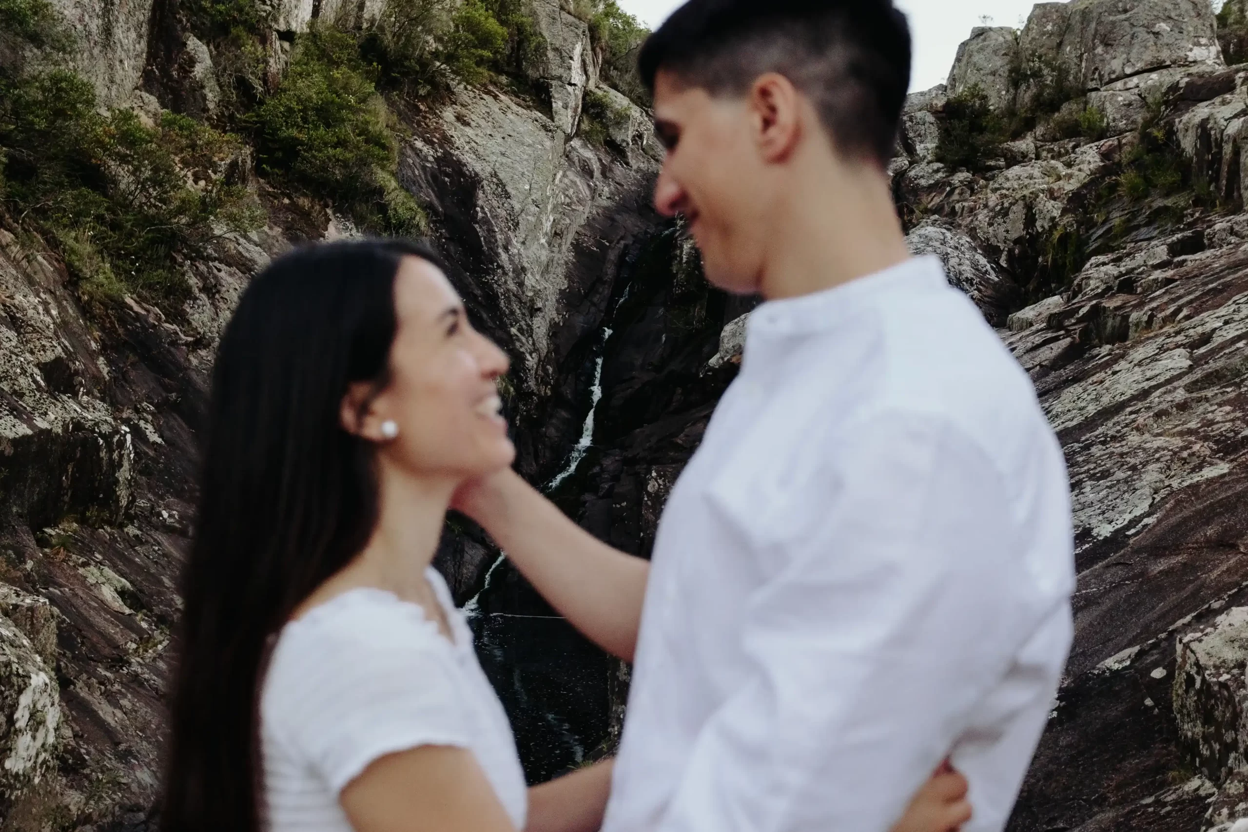 Pareja de pie juntos en un sendero rocoso rodeado de formaciones rocosas y vegetación en un paisaje montañoso al atardecer, capturados por fotógrafos de boda en Uruguay