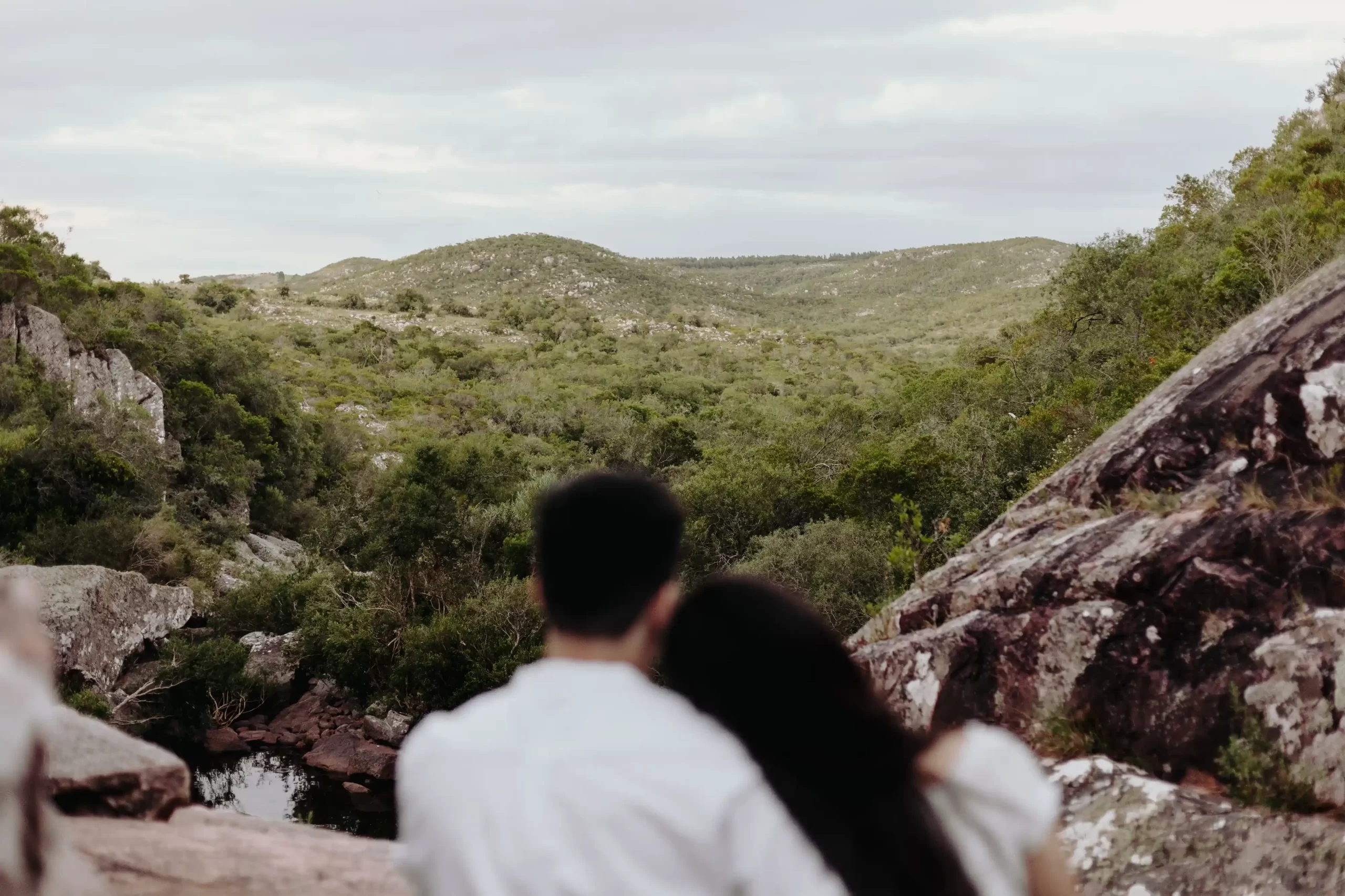 Pareja de espalda juntos en un sendero rocoso rodeado de formaciones rocosas y vegetación en un paisaje montañoso, capturados por fotógrafos de boda en Uruguay