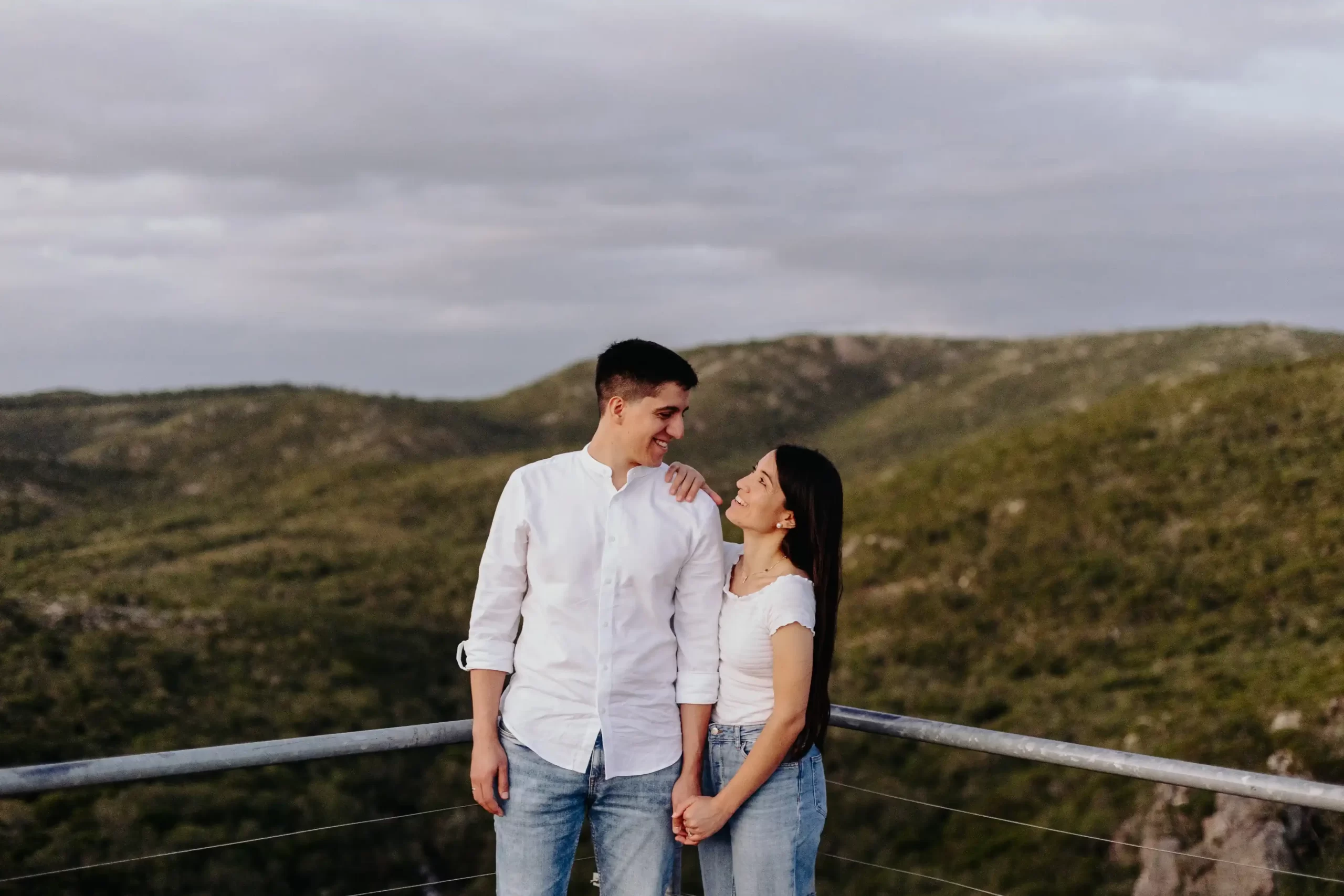 Dos personas observando un paisaje natural sereno con colinas verdes, rocas y cielo nublado, transmitiendo una sensación de tranquilidad y conexión con la naturaleza.