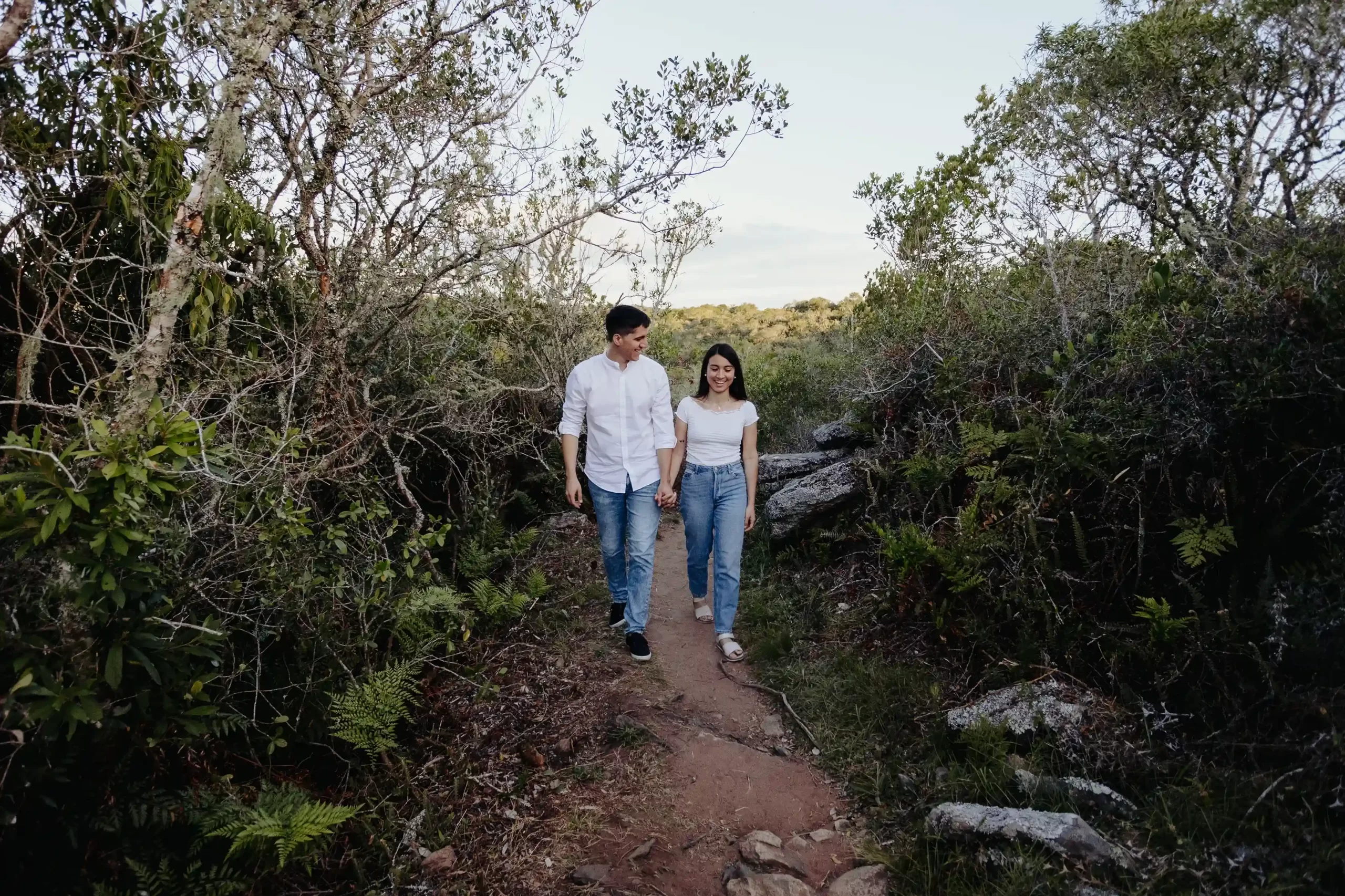 Pareja caminando de la mano por un sendero natural rodeado de vegetación, capturados en una sesión fotográfica al aire libre, ideal para fotógrafos de bodas en Uruguay