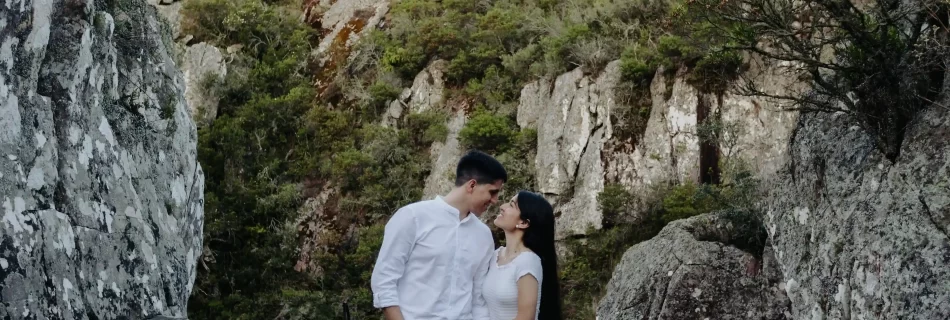 Pareja de pie juntos en un sendero rocoso rodeado de formaciones rocosas y vegetación en un paisaje montañoso al atardecer, capturados por fotógrafos de boda en Uruguay
